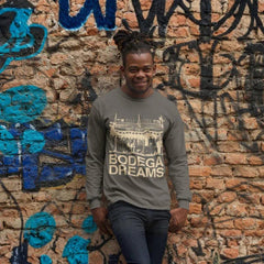 Man wearing a gray sweatshirt with 'Bodega Dreams' text against a graffiti-covered brick wall.