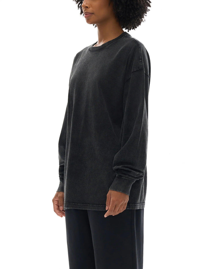 Woman wearing a loose, faded black long-sleeve crewneck shirt and black pants on white background