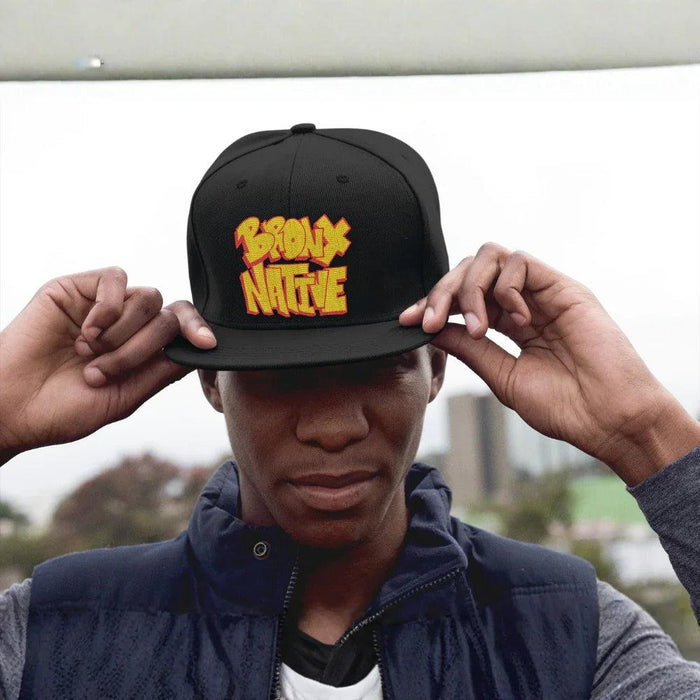 Black Bronx Native snapback hat with bold yellow-red embroidery, worn by man in urban setting